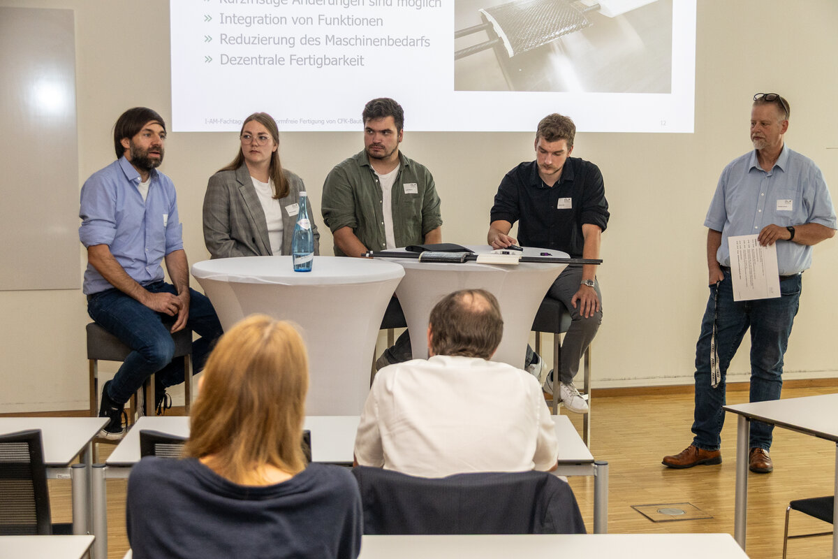 I-AM-fachtagung-podiumsdiskussion Drei Personen sitzen hinter einem Stehtisch, eine vierte steht daneben.