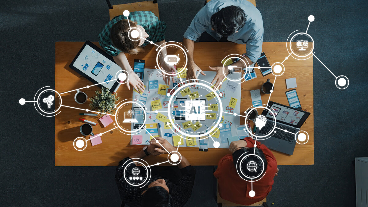 Team arbeitet an einem Tisch an digitalen Konzepten mit Fokus auf künstliche Intelligenz (AI), umgeben von Notizen, Tablets und Symbolen für Technologie und Netzwerke.