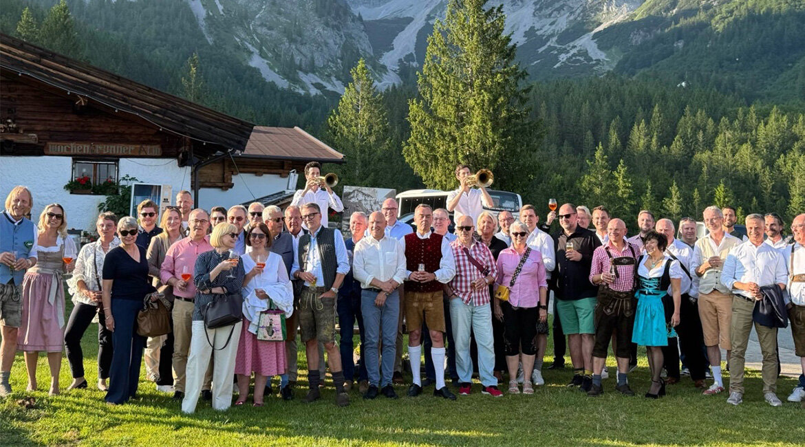 Eine Gurppe von Menschen in Tracht steht auf einer grünen Wiese vor einem hohen Berg.