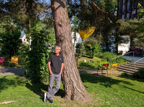 Ein Mann in Jeans und T-Shirt lehnt an einem Baum im Park. | © FH Kufstein Tirol