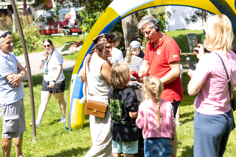ORF-Moderator im roten Poloshirt interviewt Kinder bei der Sommerfrische 2025 im Freien.