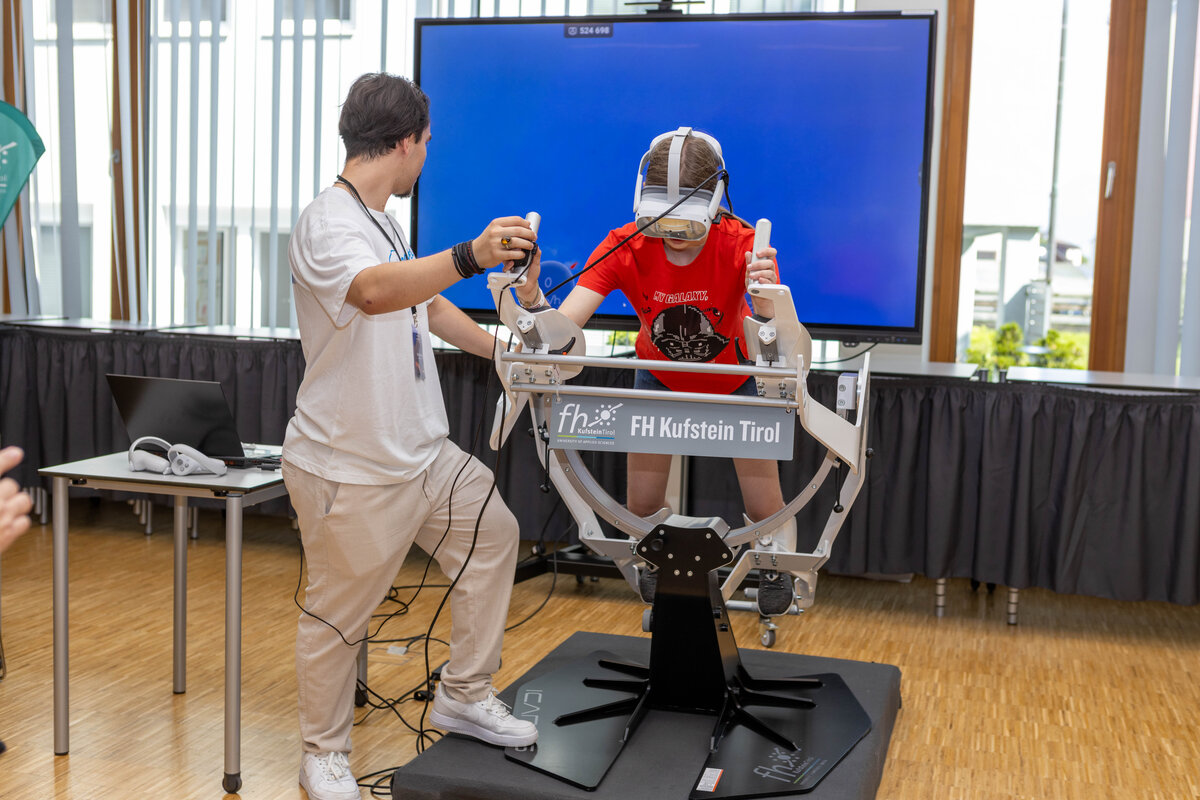 Ein Student der FH Kufstein Tirol betreut ein Kind, das mit VR-Brille und dem Flugsimulator „Icaros“ ein digitales Erlebnis ausprobiert.