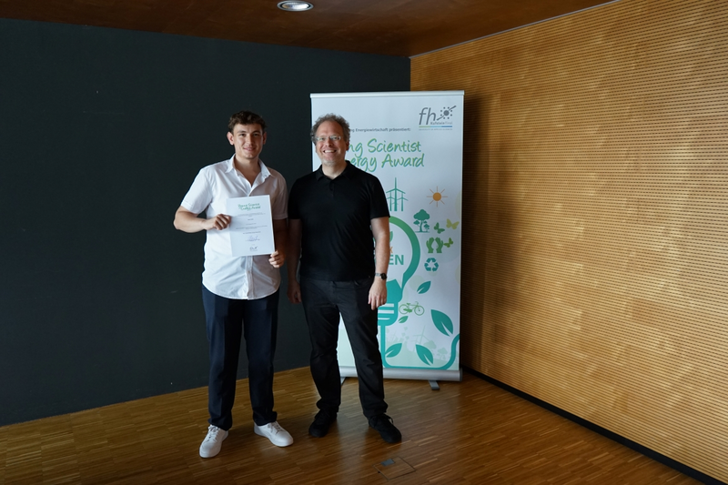 Teilnehmer des Young Scientist Energy Award mit Urkunde und Juror vor Banner.