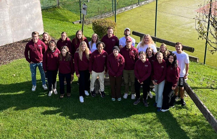Gruppenfoto von Studierenden im Freien, viele tragen bordeauxrote Kapuzenpullover mit Logo