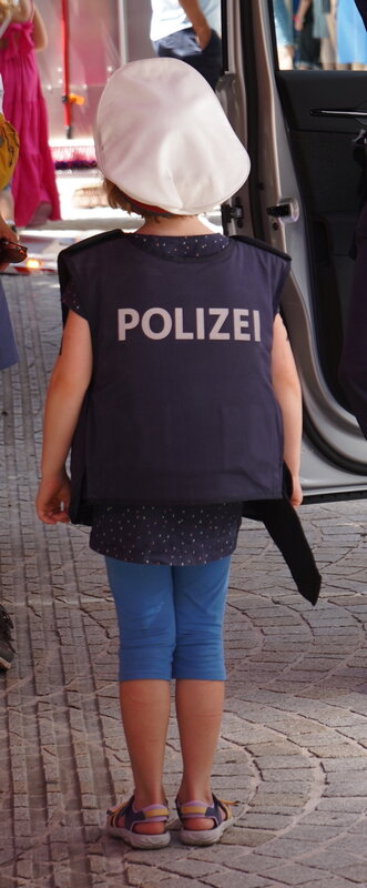 Mädchen von hinten: sie trägt eine Polizeiweste mit Hut 