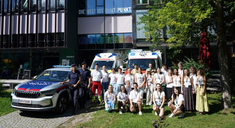 Beteiligten des Kinderliteraturfestivals stehen im Stadtpark zusammen und herum stehen Polizeiauto, Rettungswagen und Feuerwehrauto.