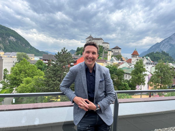 Mann in grauem Sakko steht lächelnd auf einer Terrasse im Hintergrund die Festung Kufstein und die umliegende Altstadt | © FH Kufstein Tirol