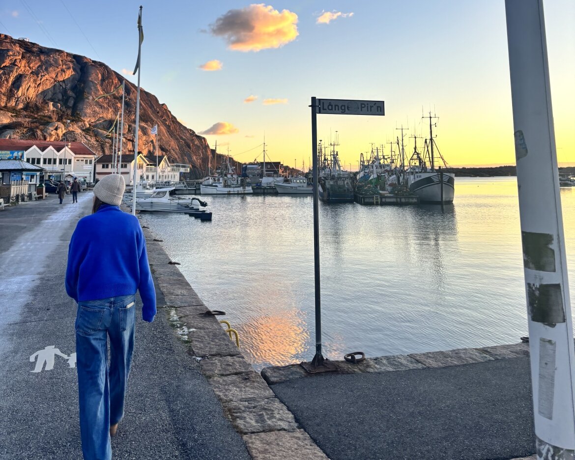 Studierende der FH Kufstein Tirol, Hanna Wimmer, bei einem Spaziergang durch die Stadt Huddingen, entlang einem kleinen Hafen mit ein paar angelegten Booten mit orange gefärbtem Himmel.