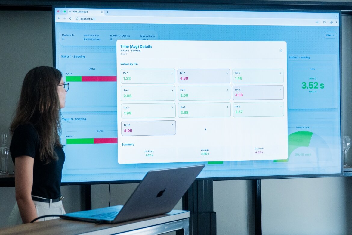 Eine Studentin aus dem Praxisprojekt der FH Kufstein Tirol bei ihrer Abschlusspräsentation im Hause der Firma 3CON, mit Blick auf einen großen Bildschirm abgebildeter Messwerte.