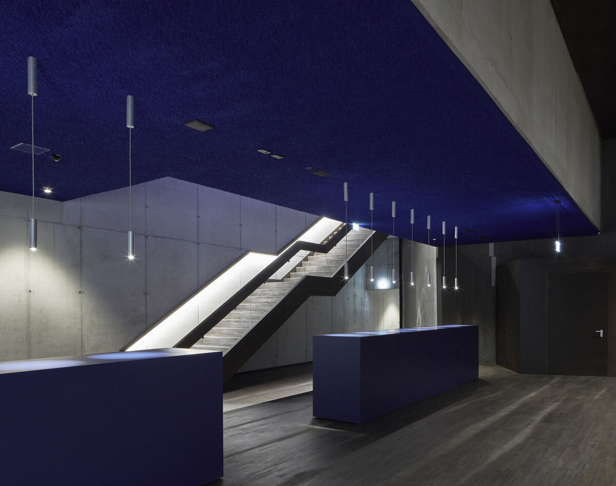 Moderner Eingangsbereich des Kultur Quartier Kufstein mit beleuchteter Treppe, minimalistischem Design und dunklen Farbakzenten.