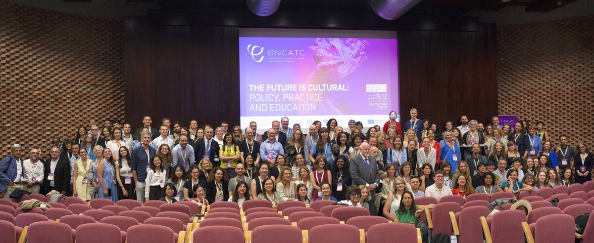 Über 100 internationale Teilnehmer:innen des ENCATC-Kongresses posieren für ein gemeinsames Gruppenfoto in einem großen Hörsaal. Im Hintergrund ist ein Screen mit dem Kongressmotto "The Future is Cultural: Policy, Practice and Education" zu sehen.