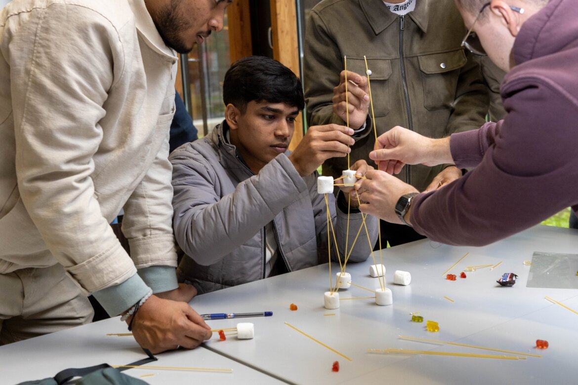 Studierende bauen gemeinsam einen Turm im Workshop Eine Gruppe von Studierenden konstruiert konzentriert einen Turm aus Spaghetti und Marshmallows im Rahmen eines interaktiven Workshops.