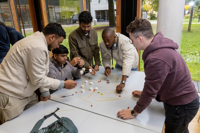 Mehrere internationale Studierende bauen im Team einen Turm aus Spaghetti und Marshmallows im Rahmen eines Workshops an der Hochschule.