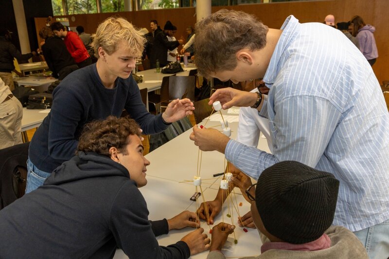 Eine internationale Studierendengruppe arbeitet konzentriert am Bau eines Turms aus Spaghetti, Marshmallows und Gummibärchen.