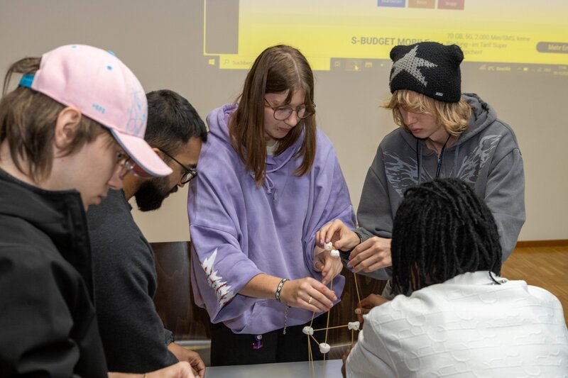 Mehrere Studierende konzentrieren sich beim Bau der Spitze eines Marshmallow-Turms während eines Gruppen-Workshops.