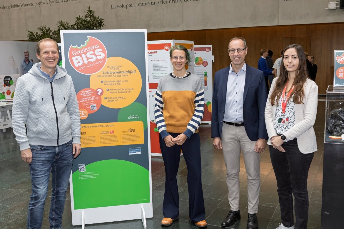 Eröffnung der Ausstellung „Gewissensbiss“ an der FH Kufstein Tirol Vier Personen stehen neben einem großen Informationsplakat zur Ausstellung „Gewissensbiss“ in der Aula der FH Kufstein Tirol. Die Ausstellung thematisiert Lebensmittelabfall und nachhaltigen Konsum. Im Hintergrund sind weitere interaktive Stationen sichtbar.