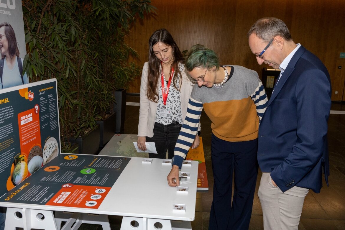 Interaktive Station der Ausstellung „Gewissensbiss“ an der FH Kufstein Tirol Drei Personen interagieren mit einer Mitmachstation der Ausstellung „Gewissensbiss“ in der Aula der FH Kufstein Tirol. Die Station beschäftigt sich mit dem Thema Schimmel und Schädlingsbefall bei Lebensmitteln.