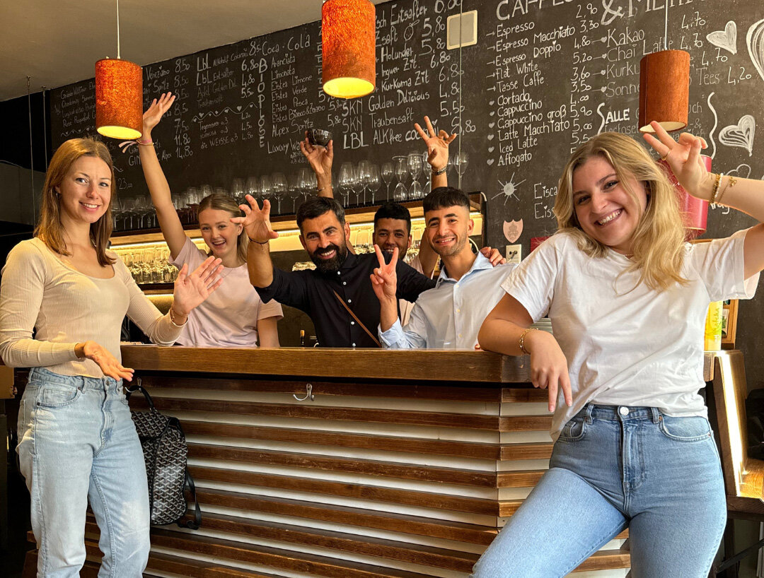 Personen stehen vor und hinter einer Theke und heben feierlich die Hände in die Luft.