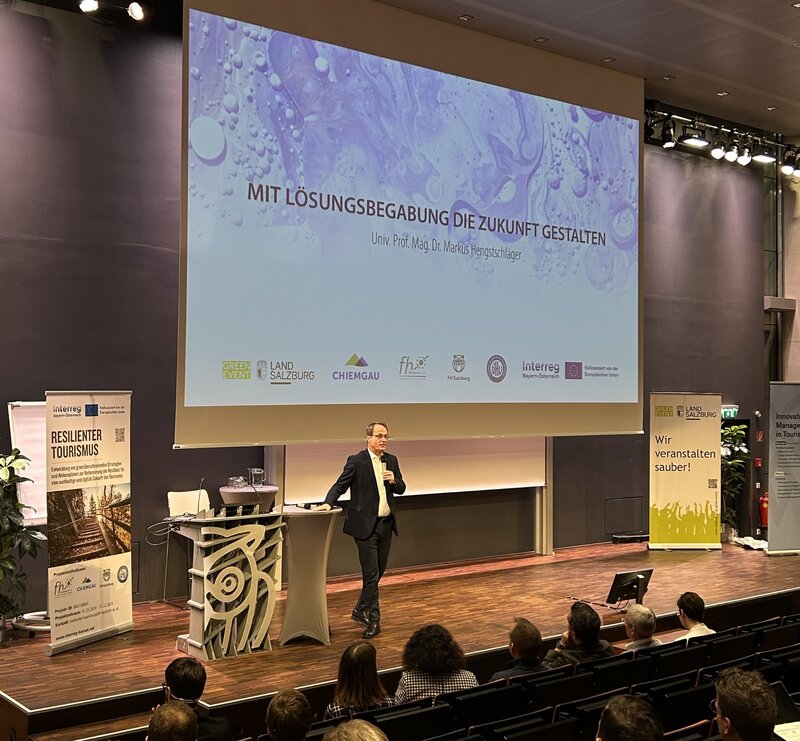 Eine Person steht auf der Bühne und lehnt sich an das Redepult.