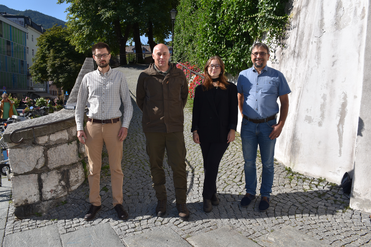Vier Mitglieder eines Forschungsteams stehen nebeneinander vor einer historischen Steinmauer in Kufstein. Im Hintergrund sind grüne Bepflanzung, Häuserfassaden und Berge zu sehen.