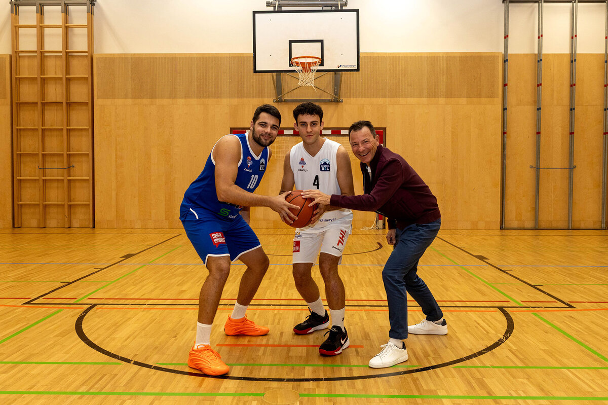 Drei Personen stehen auf dem Basketballfeld und halten ihre Hände auf einen Basketball und schauen in die Kamera.