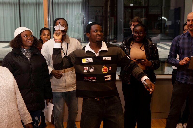 Personen stehen um einen Mann der gerade versucht einen Papierflieger zu werfen.