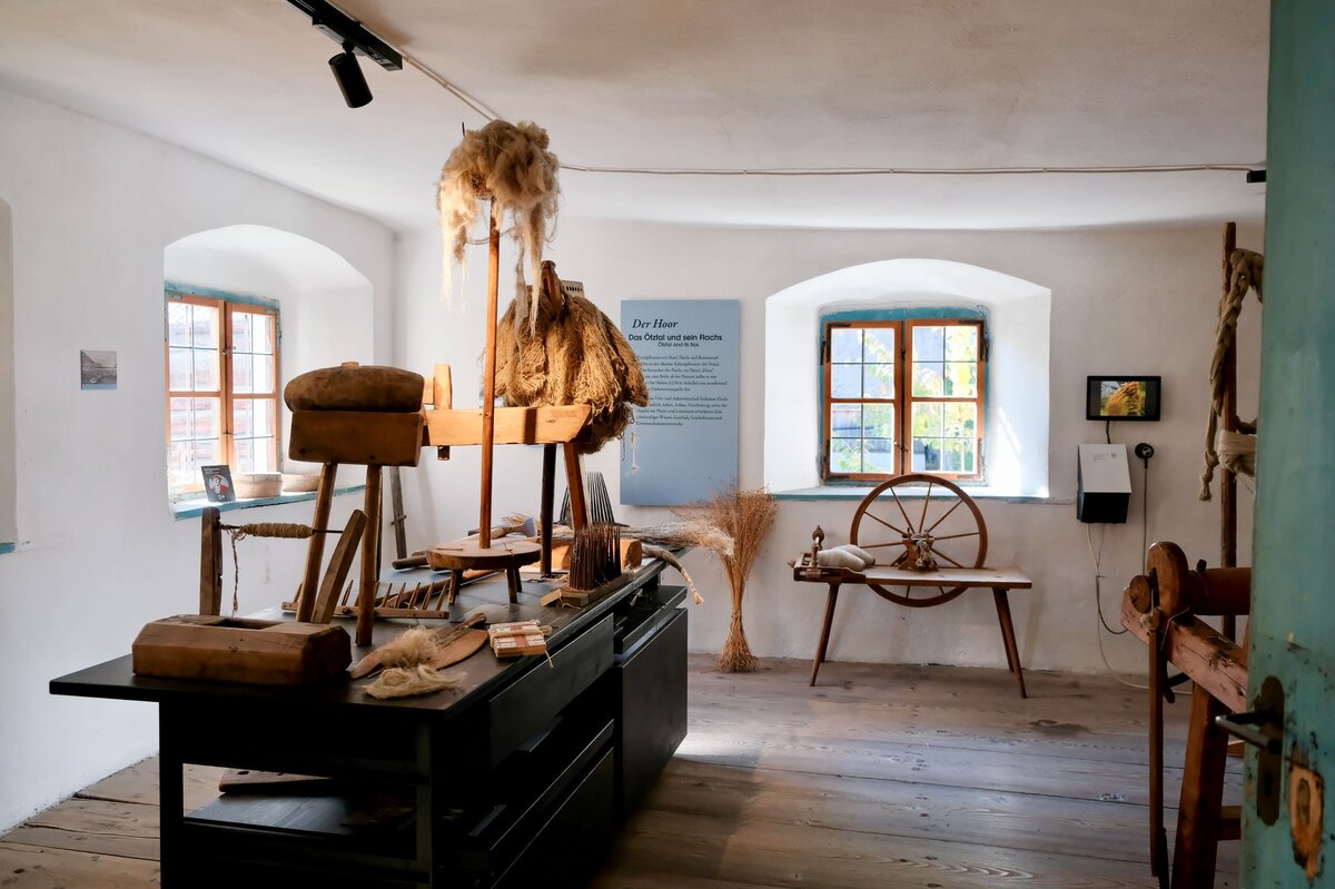 Ein Raum mit einem Spinnrad, einem Holztisch und verschiedenen anderen Gegenständen.
