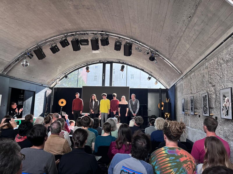 Blick hinter dem Publikum auf die Bühne.