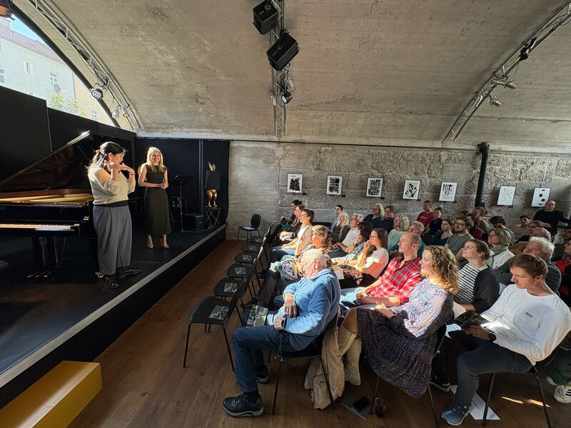 Zwei Personen stehen auf einer Bühne und sprechen zum sitzenden Publikum.