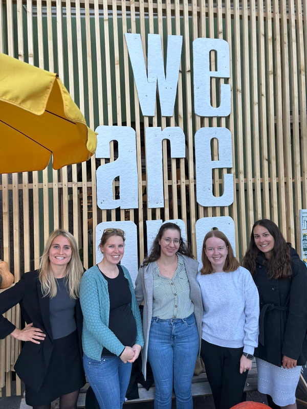 Personen stehen vor einer Wand aus Holz nebeneinander.