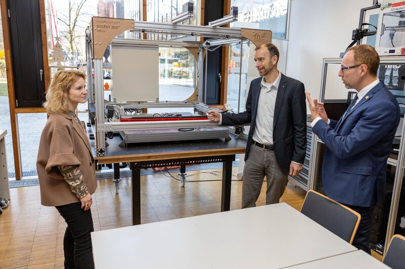 Drei Personen stehen vor einer Maschine und erklären die Funktion.