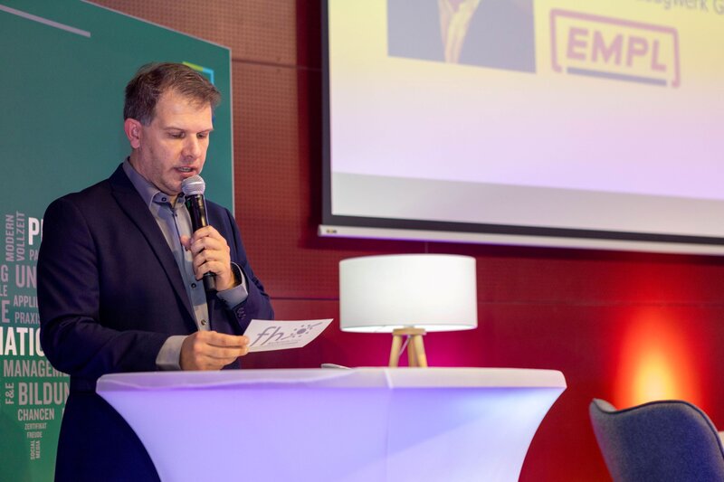 Person steht an einem Tisch und hält das Mikrofon an den Mund.