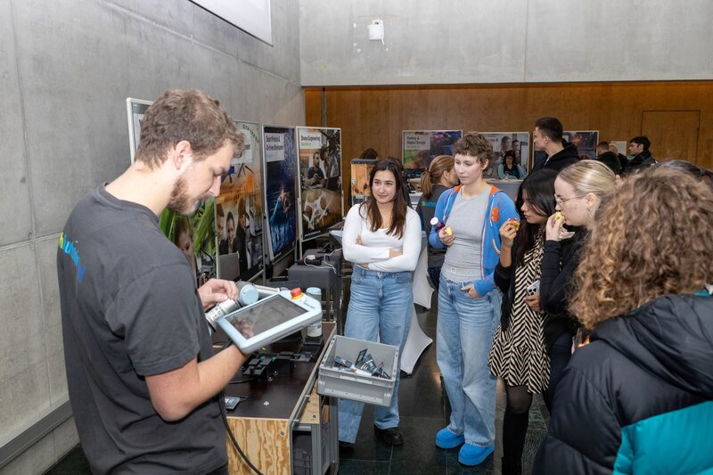 Personen stehen um den Tisch und blicken auf die erklärende Person.