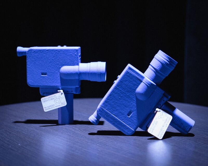 Zwei blaue Skulpturen einer Kamera stehen auf einem Tisch.