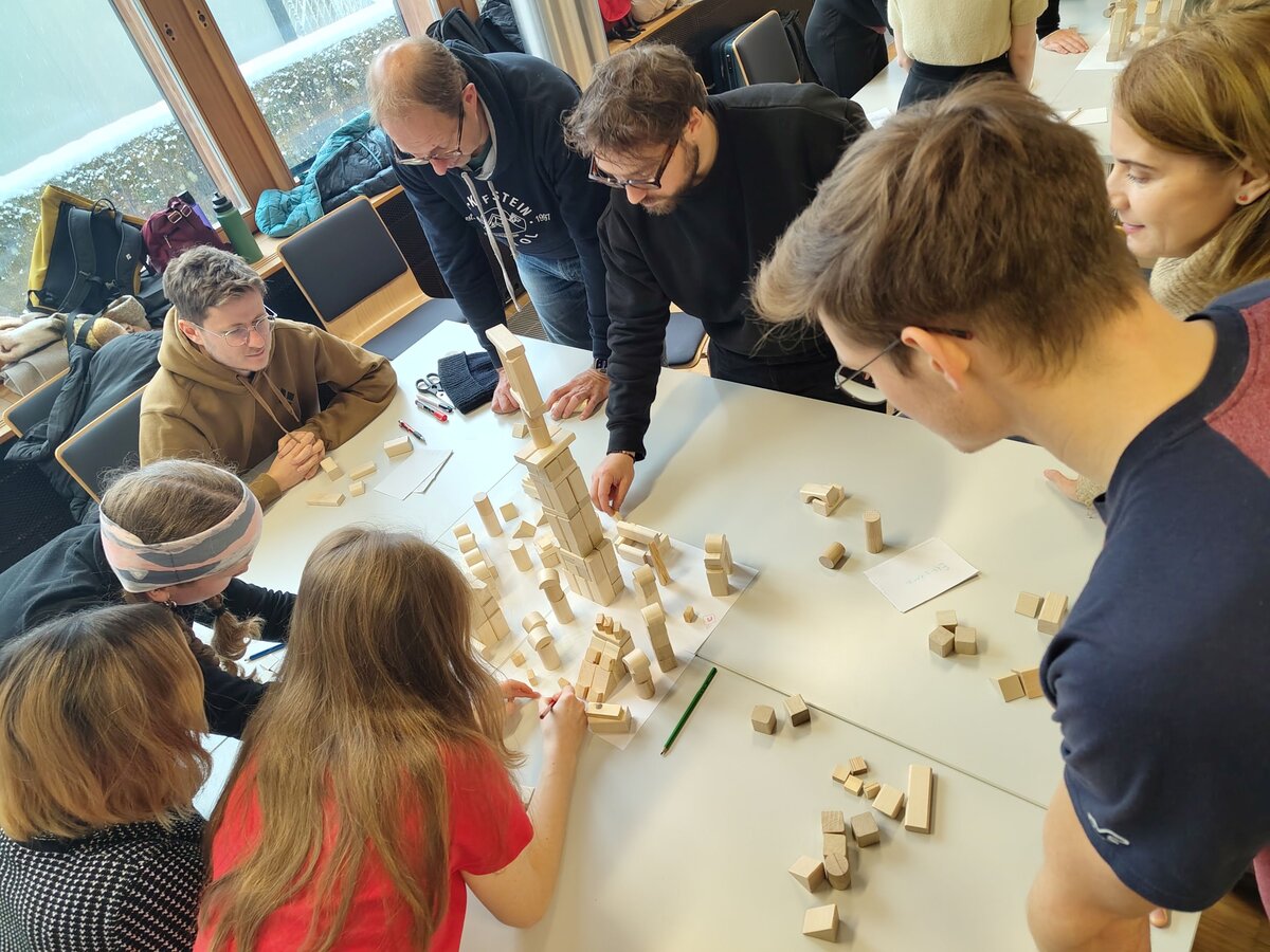 Personen stehen um einen Tisch herum und bauen mit Holzklötze einen Turm.