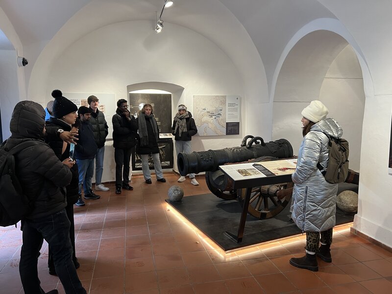 Personen stehen in einem Raum mit ausgestellten Waffen.