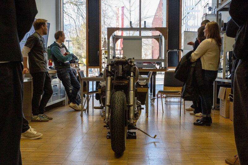 In der Mitte von einem Personenkreis steht ein altes Motorrad.