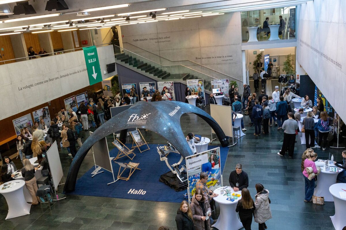 Blick von oben auf die Aula der FH Kufstein Tirol - mit Informationsständen im Raum verteilt.