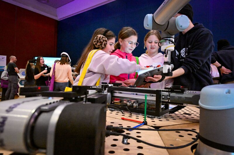 Drei Mädchen stehen an der Station und probieren den Roboterarm aus.