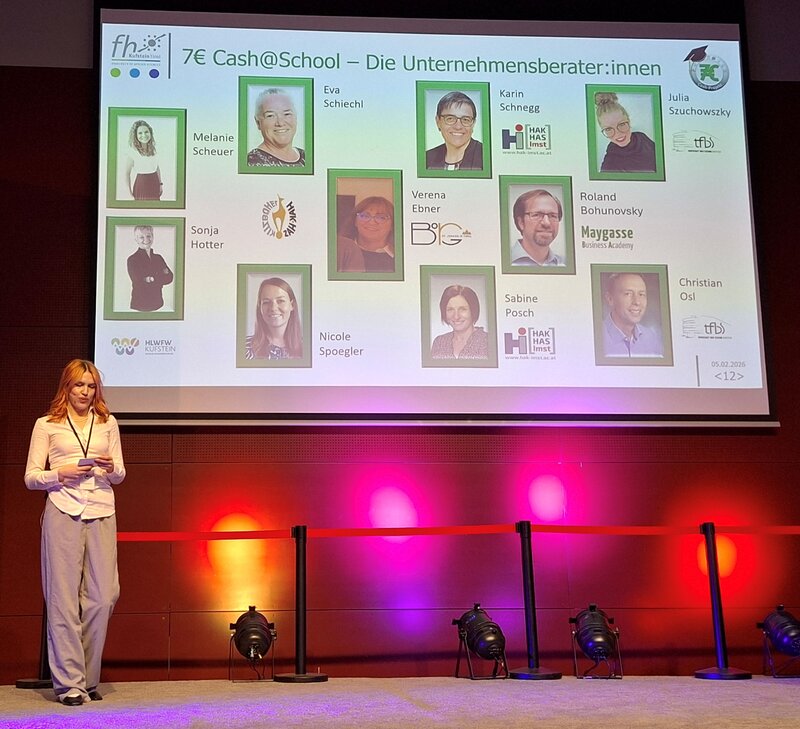 Moderatorin steht auf der Bühne und stellt Lehrer:innen als Unternehmensberater:innen vor. 