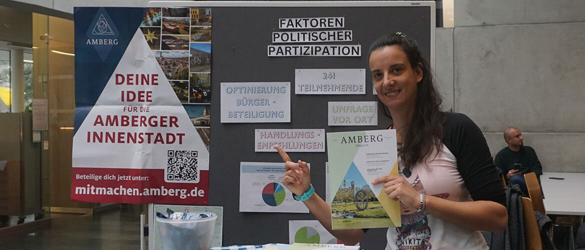 praxisprojekt_buergerinnenbeteiligung Eine Studentin präsentiert ihre Ergebnisse auf einer Plakatwand in der Aula der FH Kufstein Tirol.