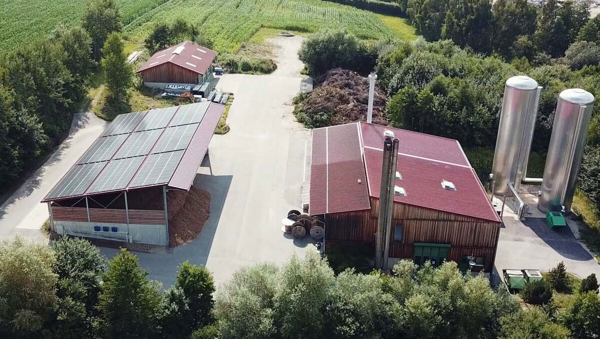 Luftaufnahme des Biomasse-Heizwerks Rinning der Stadtwerke Dorfen mit roten Dächern und zylindrischen Silos, umgeben von Grünflächen.