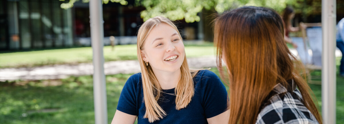 Park_Duo_sitzend | © FH Kufstein Tirol Zwei Frauen sitzen im Park und halten eine fröhliche Konversation miteinander. | © FH Kufstein Tirol