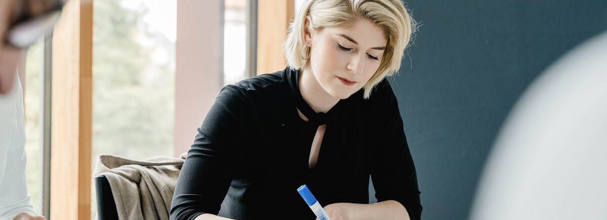 Frau_plant_Präsentation | © FH Kufstein Tirol Eine Frau schreibt etwas auf ein rundes Stück Papier. | © FH Kufstein Tirol
