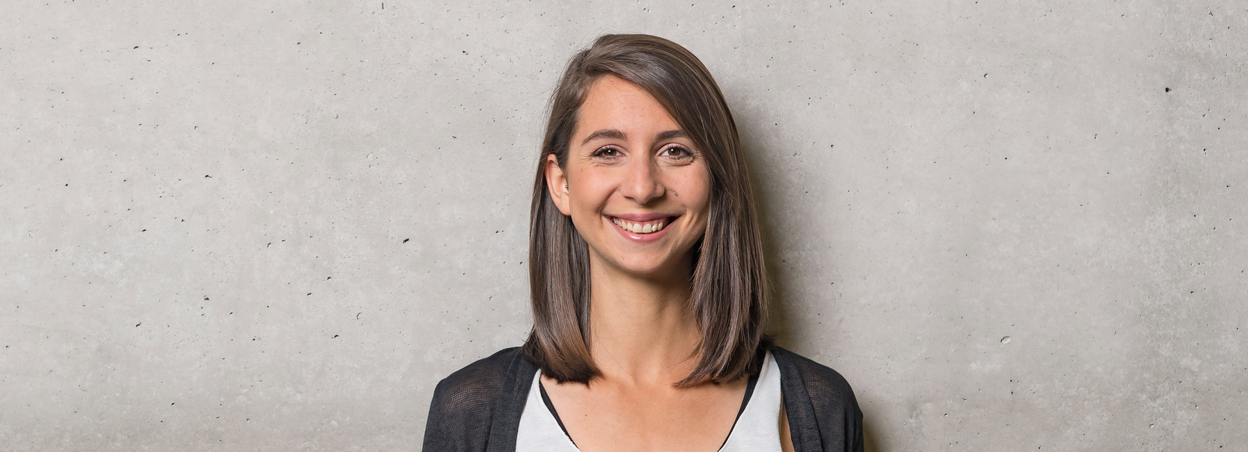 BA_CODE_VZ | © FH Kufstein Tirol Eine Frau steht mit dem Rücken zu einer grauen Wand und blickt lächelnd in die Kamera. | © FH Kufstein Tirol