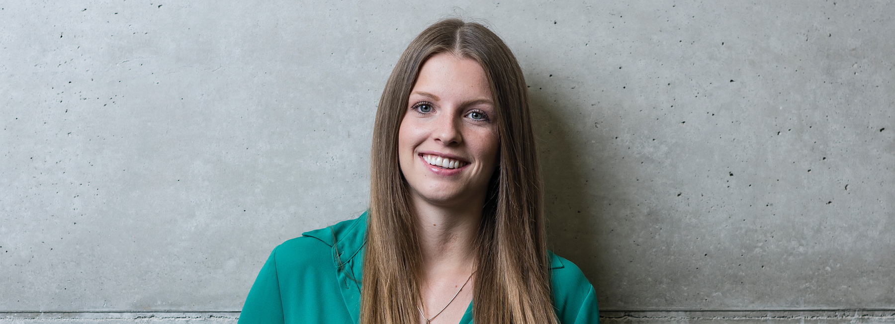 MA_ERP_BB | © FH Kufstein Tirol Eine Frau steht mit dem Rücken zu einer grauen Wand und blickt lächelnd in die Kamera. | © FH Kufstein Tirol