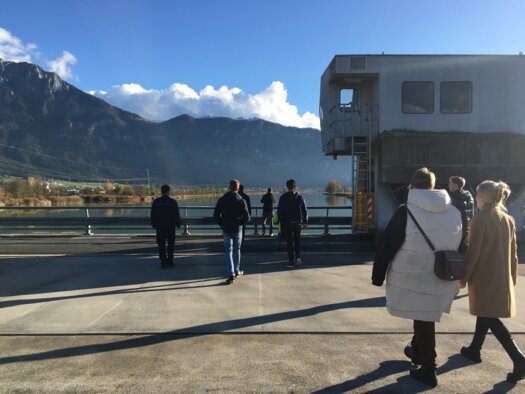 Studierende gehen auf dem Staudamm und betrachten das Wasserkraftwerk